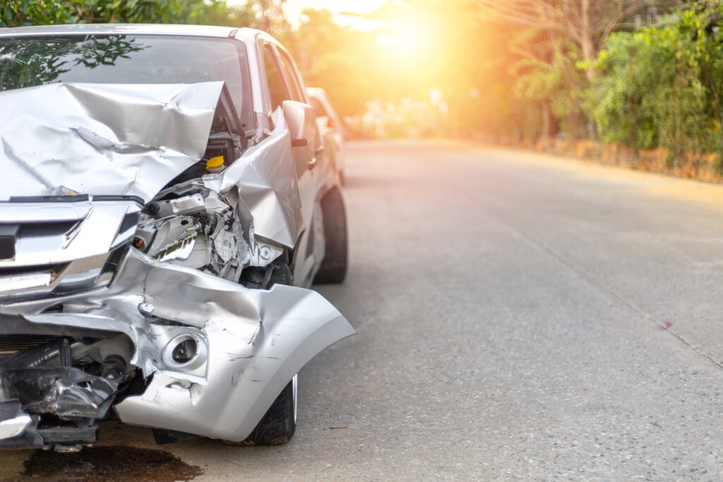 Front of light gray color car, damaged and broken by accident on road in morning time.