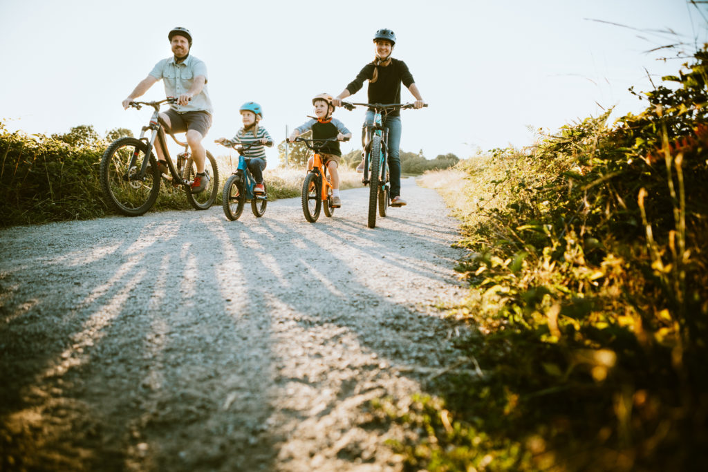 A father and mother ride bikes with their children. Each is wearing a helmet to avoid accidents.